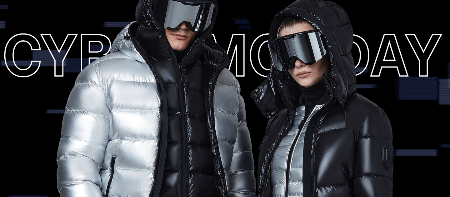 Two models in shiny winter jackets and large futuristic sunglasses pose against a black background with “CYBER MONDAY” text partially visible behind them. One jacket is silver, the other is black.