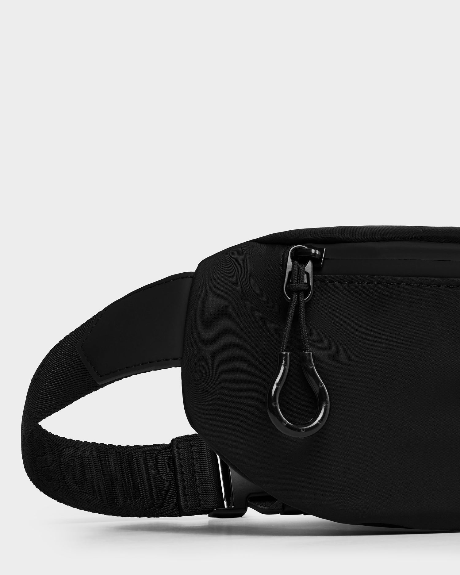 Close-up of the Rudsak RILO - 9326000 Black waist bag featuring a zippered pocket, visible strap, and black buckle against a plain light background.