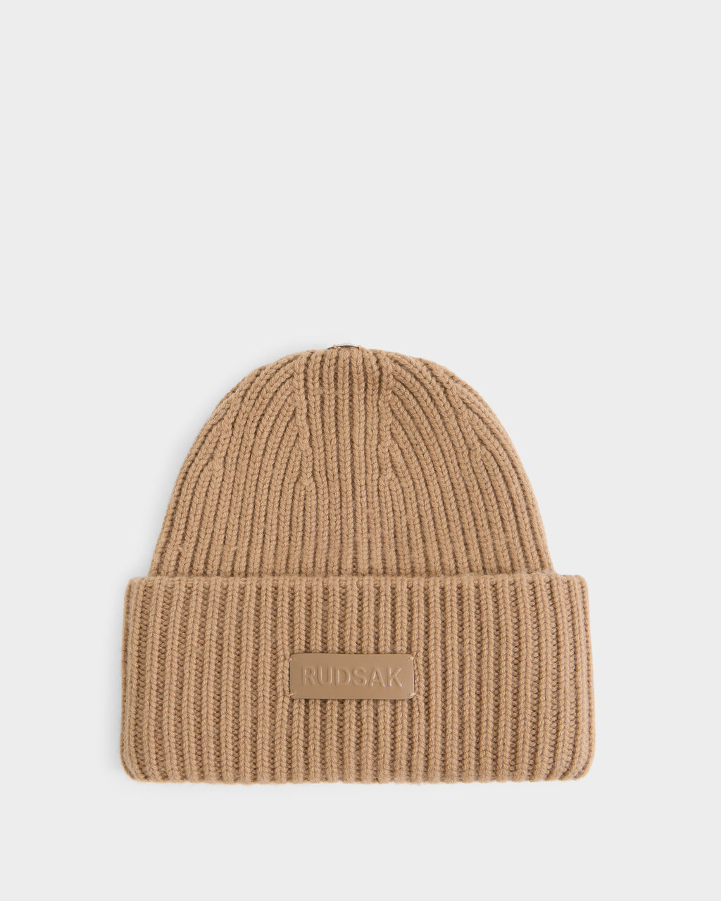 Introducing the DARA - 8425019 Camel beanie by Rudsak: a beige, ribbed knit design featuring a folded brim and a rectangular RUDSAK patch on the front, showcased against a plain white background.