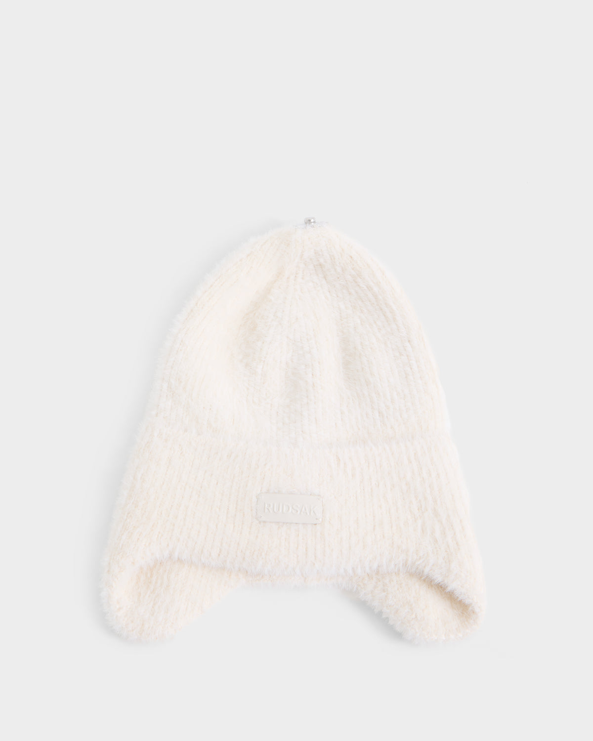 A soft, white knit beanie with ear flaps and a small rectangular patch on the front, the Rudsak ICE - 8426519 Vanilla, is displayed on a plain white background.