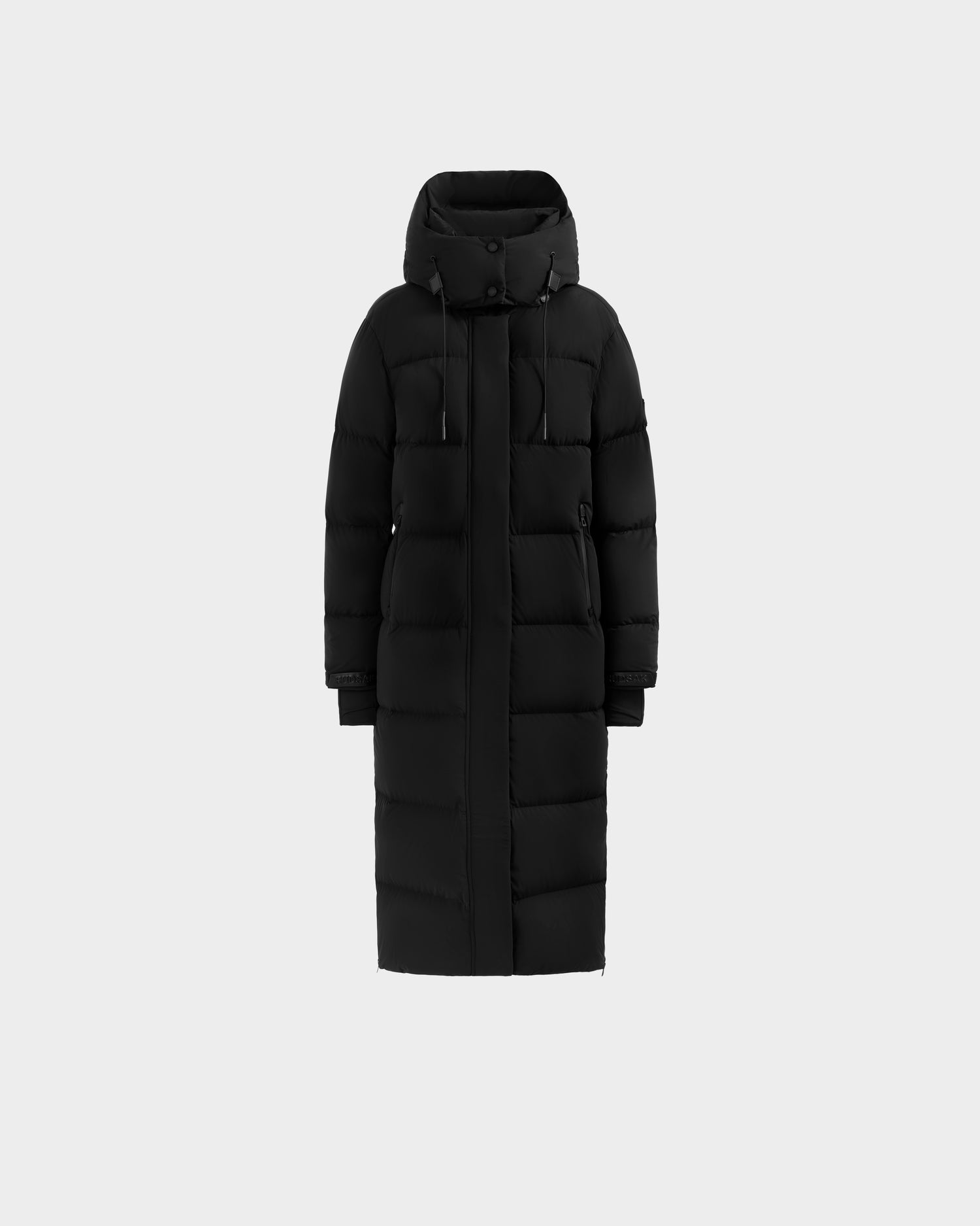 Rudsak's ALESSANDRA L - L125553 Black is a long black quilted down puffer coat with a hood, front zipper, snap buttons, and two side pockets, shown against a light gray background—a true winter essential.