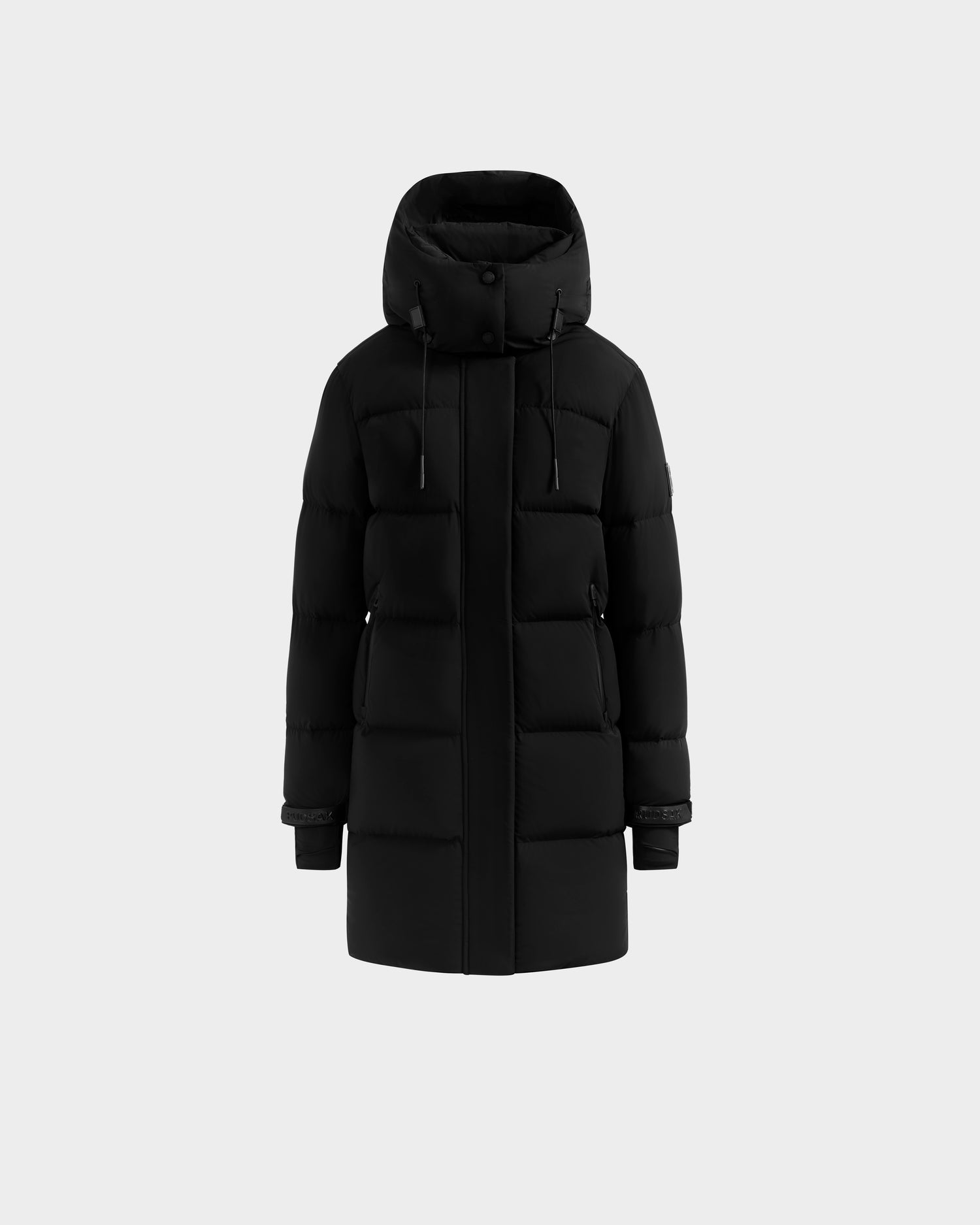 The Rudsak ALESSANDRA M - L125552 Black is a long women’s matte down puffer with a hood, front zipper, snap buttons, horizontal stitching, adjustable cuffs, and cozy insulation for warmth. Shown on a plain light gray background.
