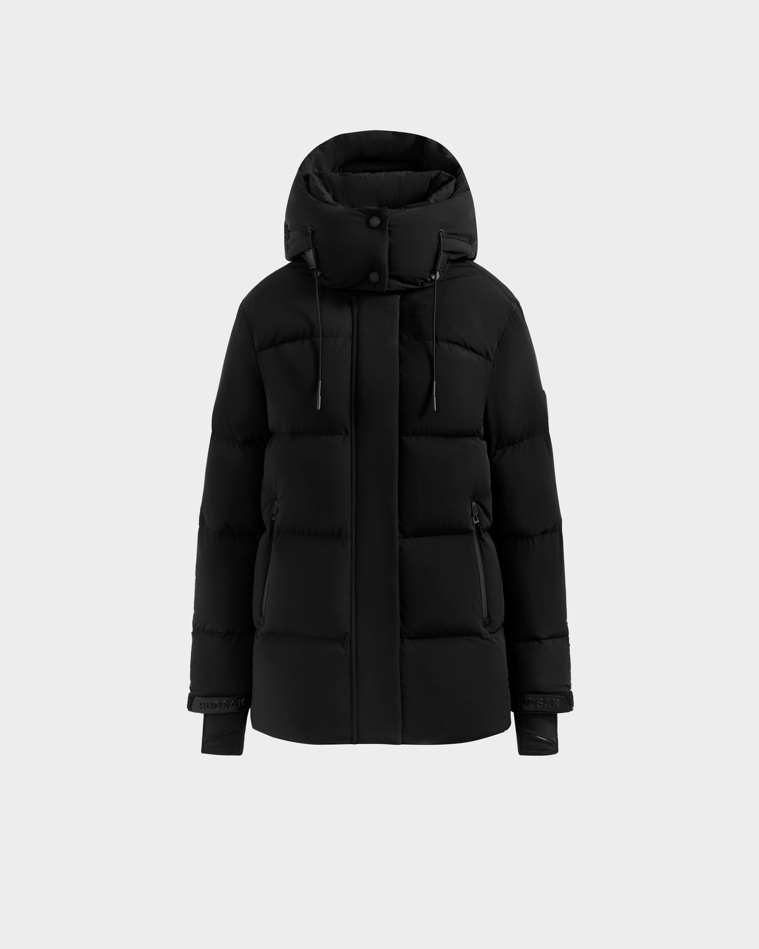 The Rudsak ALESSANDRA S-M - L125551 Black is a black puffer jacket with high collar, removable hood, front zipper, snap buttons, two side pockets, and adjustable drawstrings, shown against a plain light gray background.