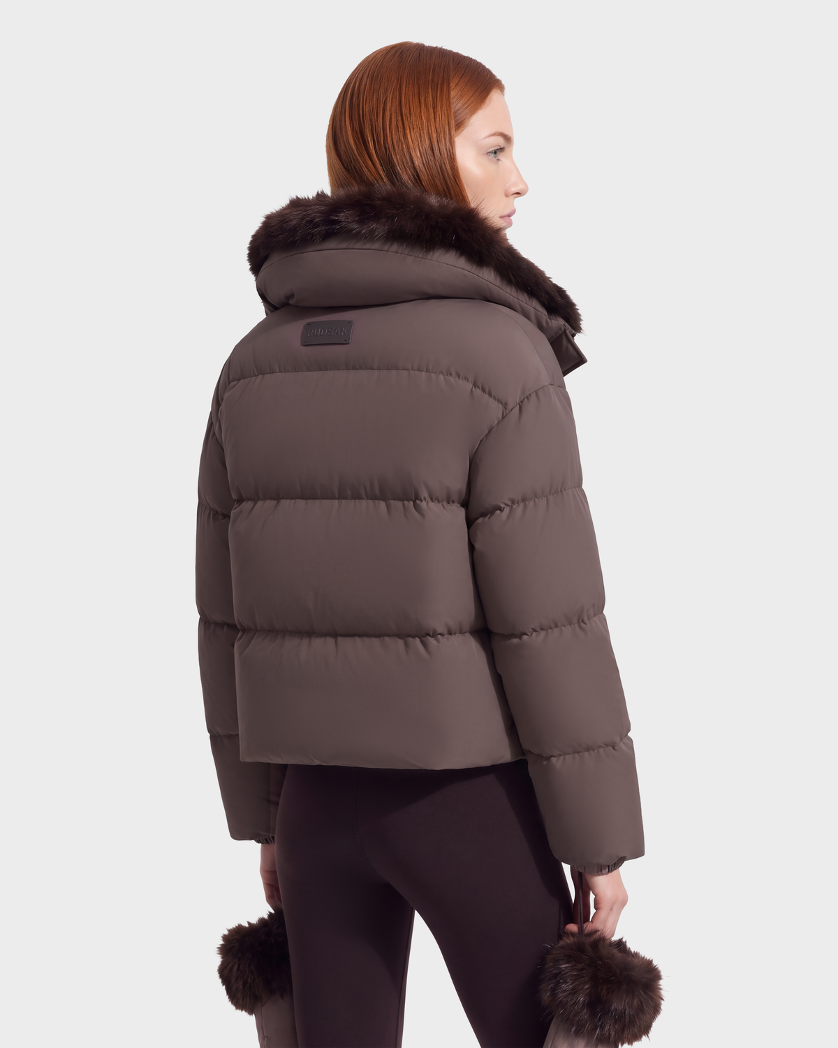 A person viewed from behind wearing the ALONDRA - 8126992 Espresso, a brown cropped puffer jacket with a fur-trimmed collar and fur-trimmed sleeve cuffs.