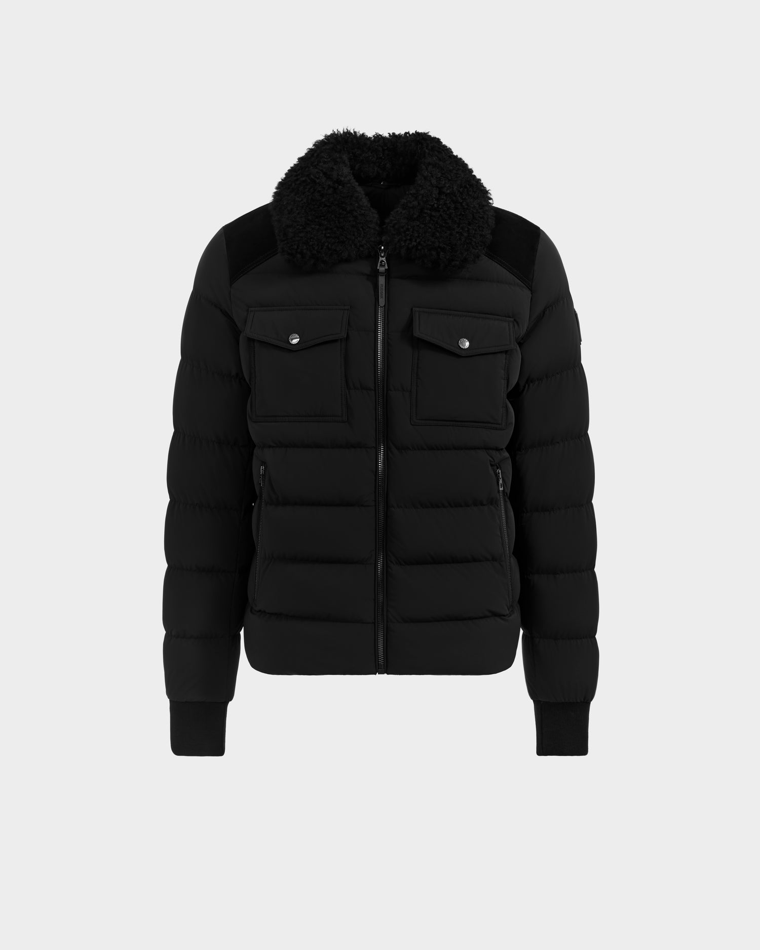 The Rudsak ANTHONY - 6125042 Black men’s aviator jacket features a front zipper, two chest flap pockets with buttons, ribbed cuffs and hem, and a wide black shearling collar, shown on a plain light gray background.