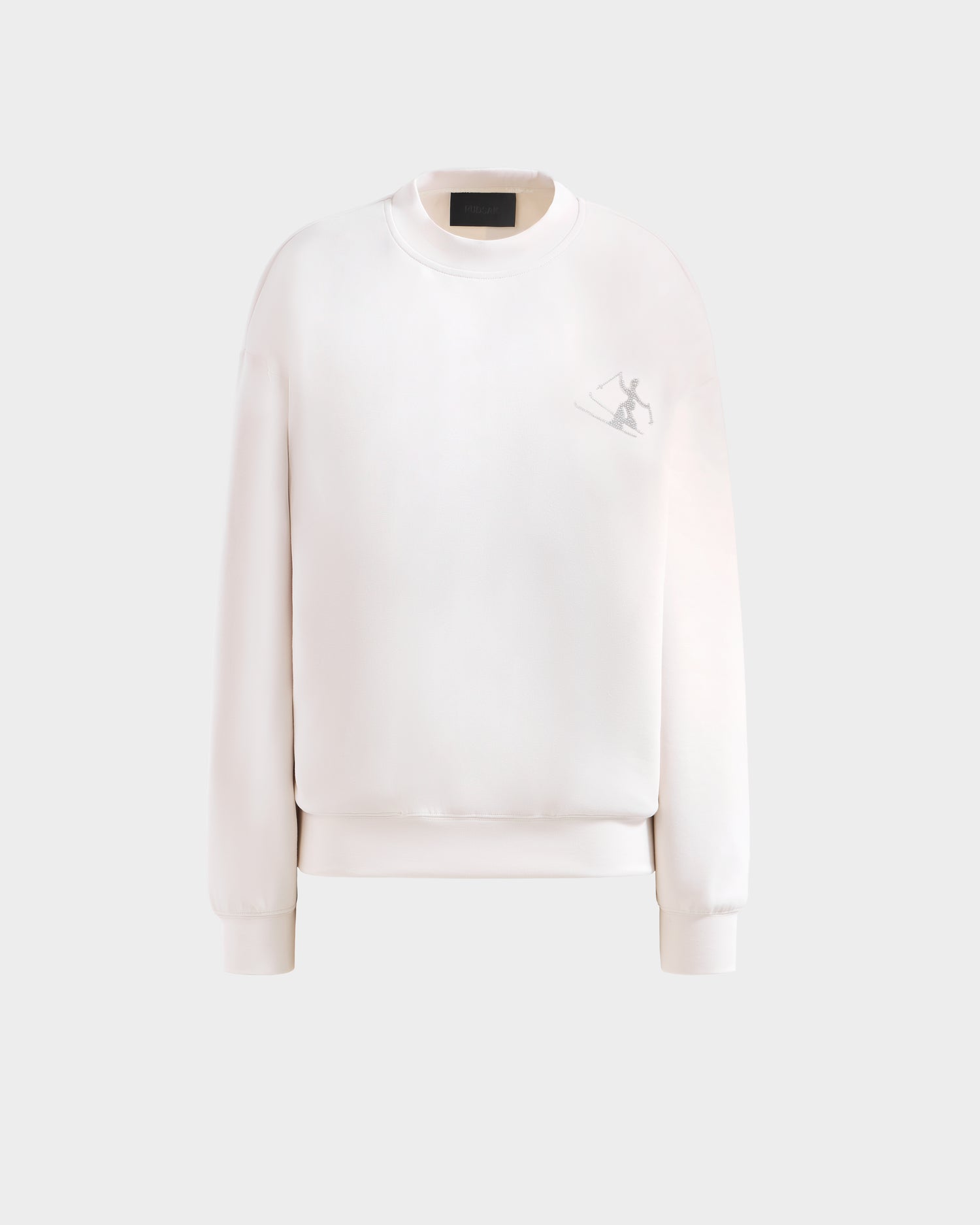The Rudsak ARIA - 8525661 Vanilla is a plain white women’s crewneck sweatshirt with ribbed cuffs and hem, featuring a small rhinestone ski figure graphic on the upper left chest, shown against a light gray background.