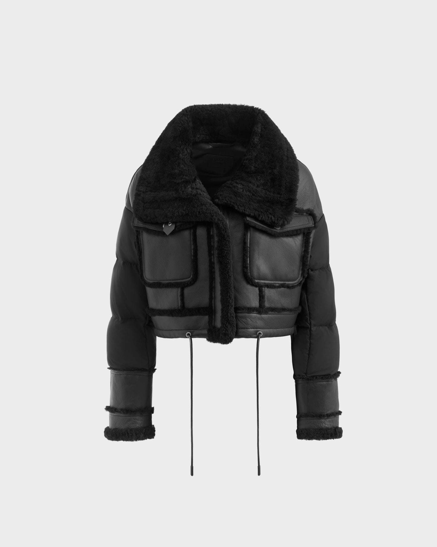 The ARIELLA - 8125505 Black by Rudsak is a cropped womens shearling puffer jacket with a wide faux fur collar, down-filled sleeves, two large front pockets, faux fur cuff trim, and black drawstrings at the hem. Shown on a plain light background.