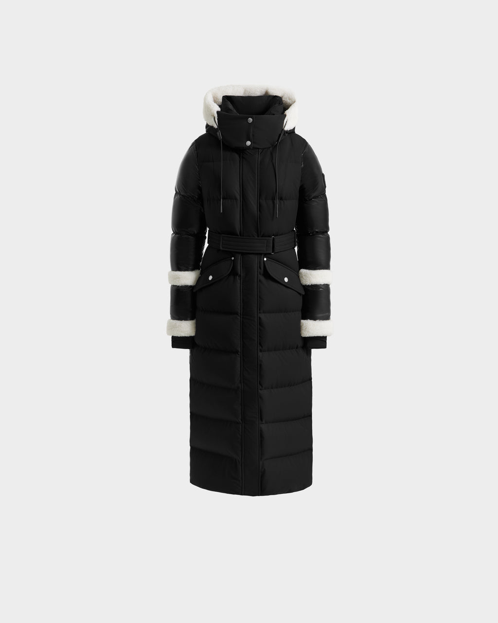 The AUDREY XL - 8125601 Black/Iceland by Rudsak is a maxi-length down puffer jacket with a belted waist, high collar, hood and cuffs lined in white faux fur, plus two front snap-closure pockets for winter warmth.
