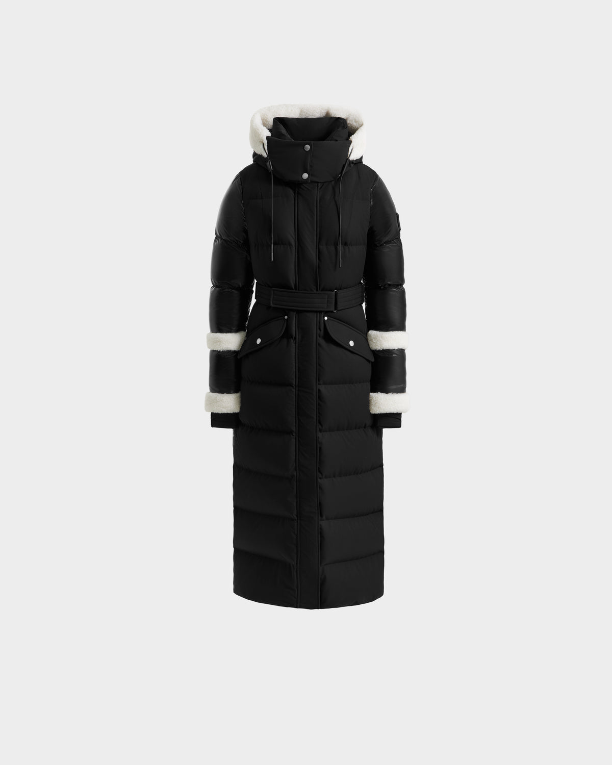 The AUDREY XL - 8125601 Black/Iceland by Rudsak is a maxi-length down puffer jacket with a belted waist, high collar, hood and cuffs lined in white faux fur, plus two front snap-closure pockets for winter warmth.