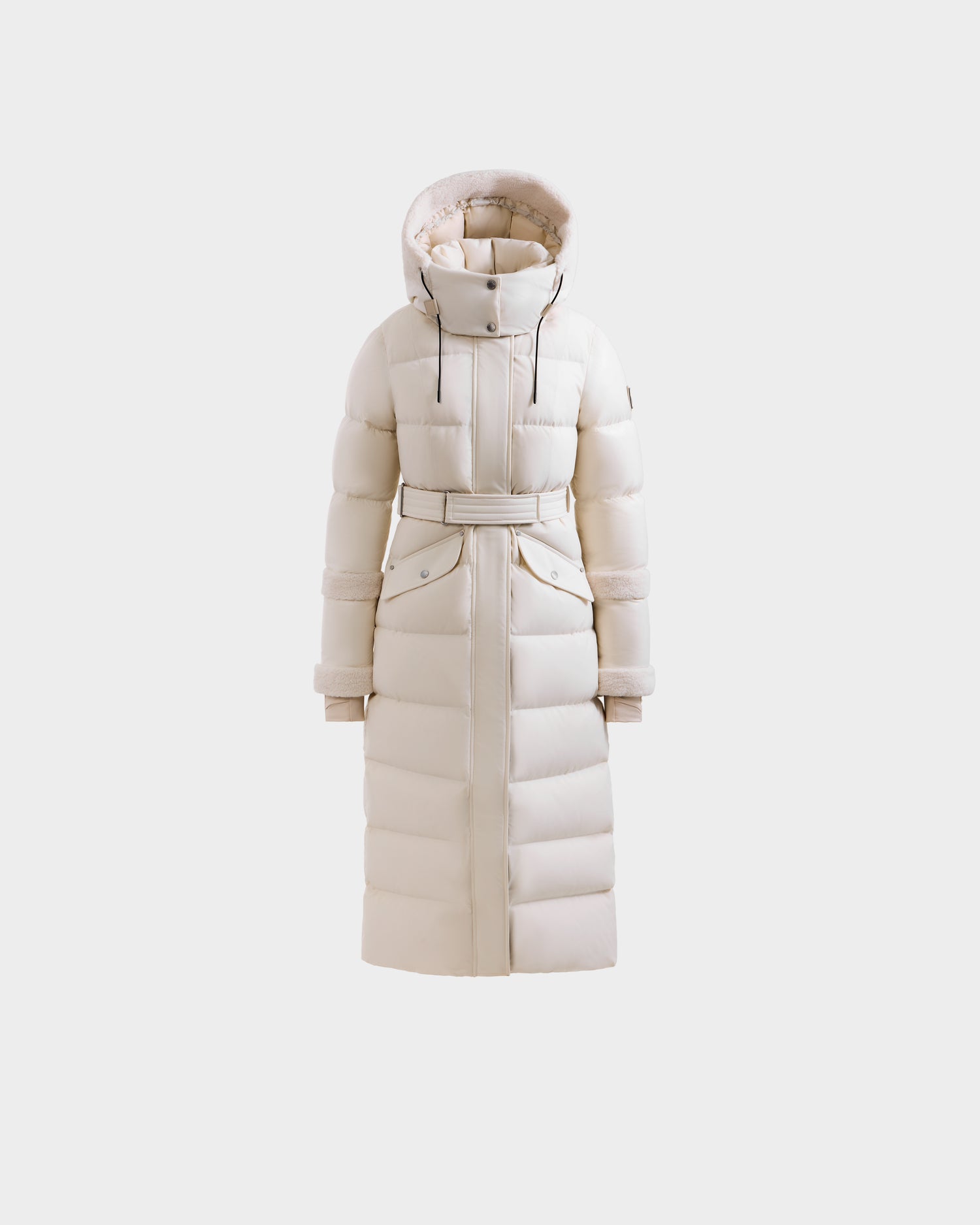 The Rudsak AUDREY XL - 8125601 Vanilla is a cream maxi-length down puffer jacket with a belted waist, large hood, front pockets, and quilted design, shown on a plain white background.
