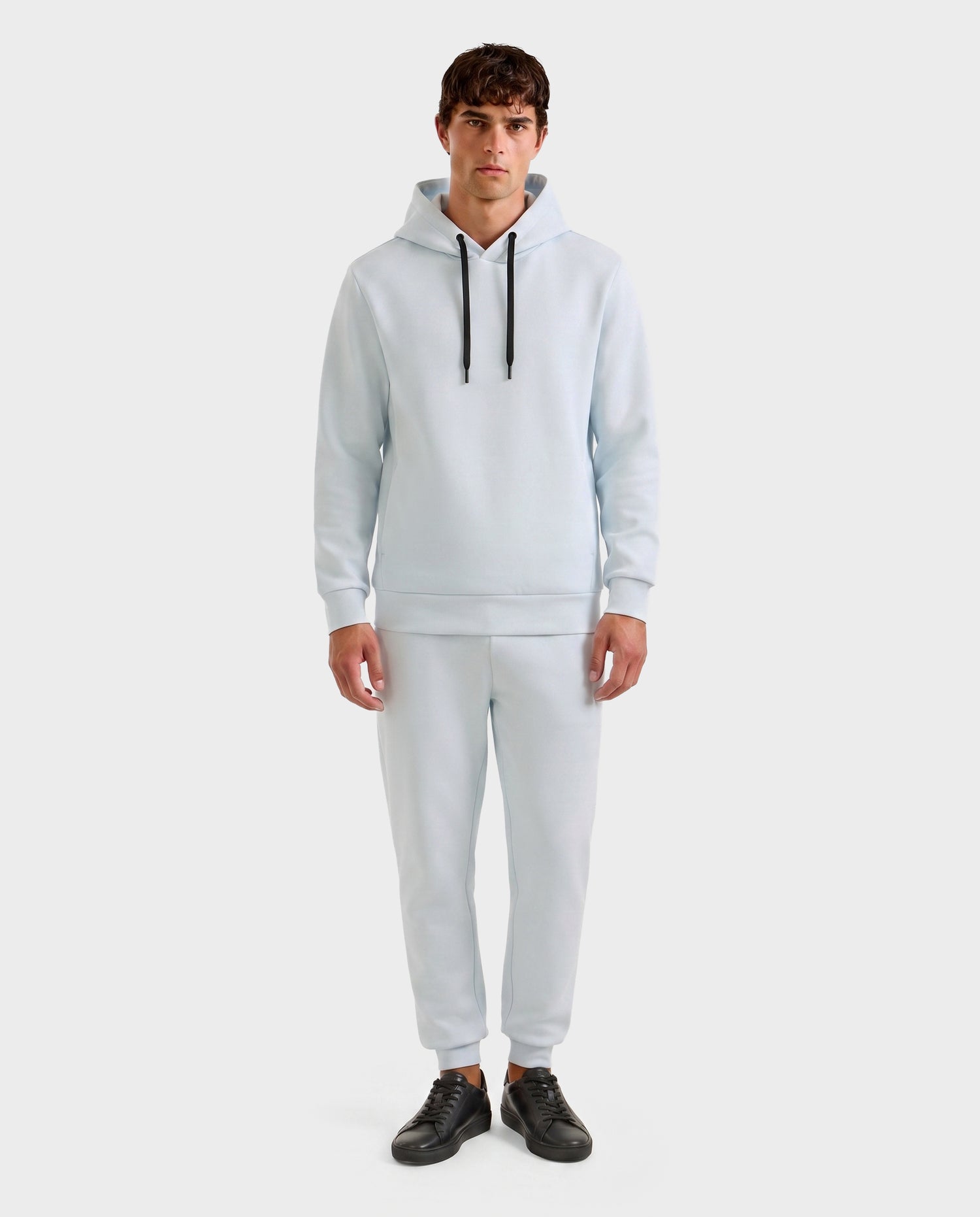 A man faces forward wearing the Rudsak LEROY - U525509 Sky Blue M premium unisex hoodie with black drawstrings and matching jogger pants, paired with black sneakers, set against a plain white background.