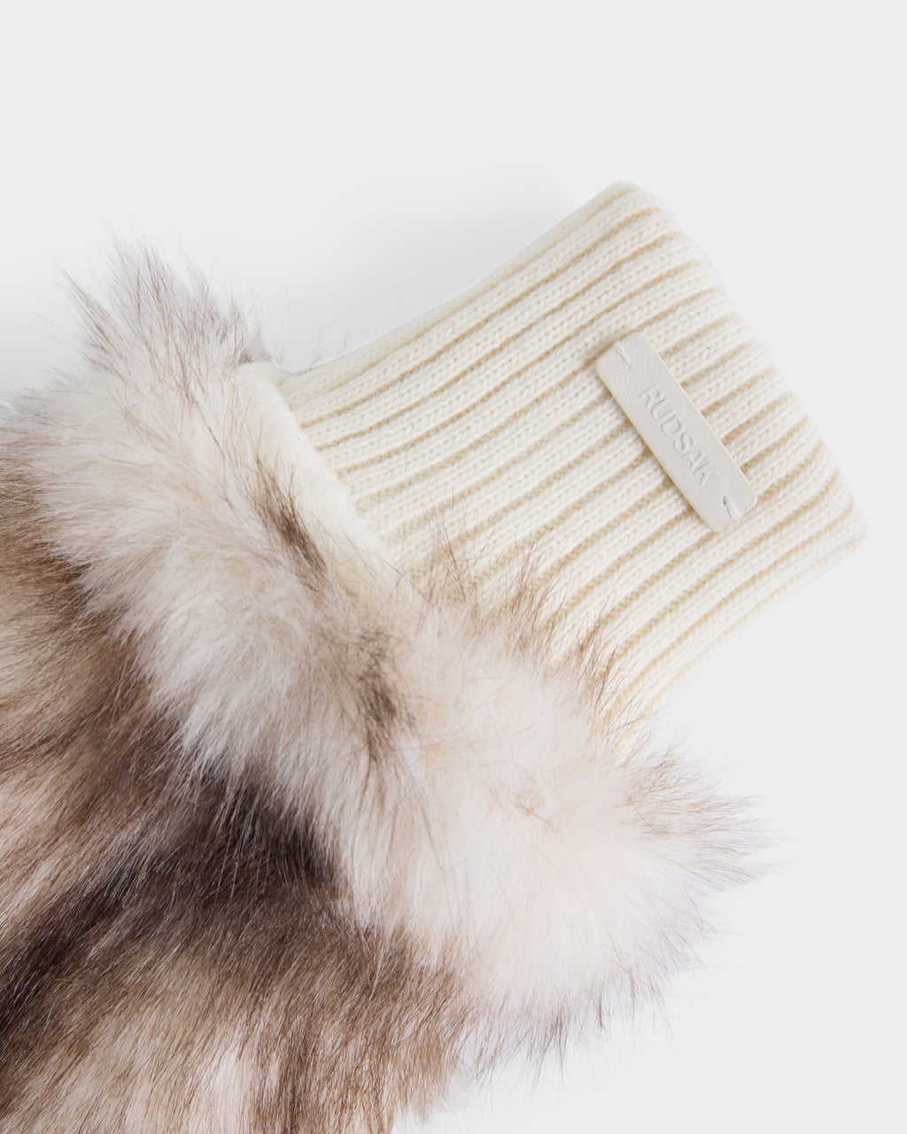 A close-up of the BELLA - 8425006 Mix Vanilla mitten by Rudsak showcases its cream-colored, ribbed knit cuff with a signature RUBASHKA label and a trim of soft, light brown and white faux fur—an elegant detail that transforms these mittens into must-have winter accessories.