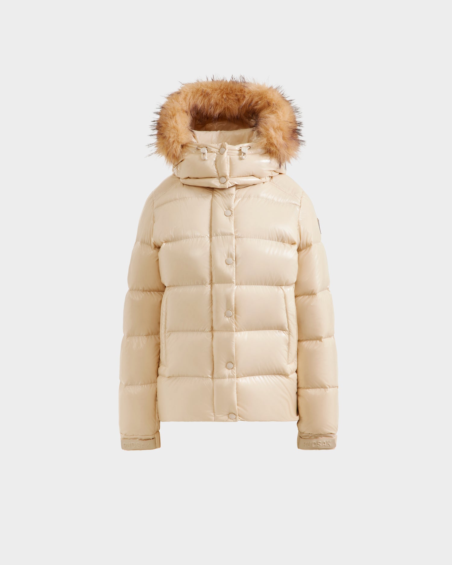 The Rudsak BREE S - L125583 Vanilla is a stylish beige women’s down puffer jacket with a front button closure, two side pockets, and a brown faux fur-trimmed hood, featured as weather-resistant outerwear on a white background.
