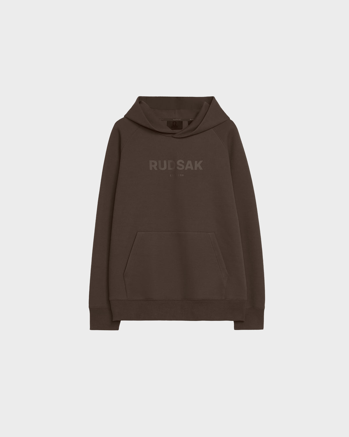 The Rudsak BRIAR - 9525001 Espresso W is a dark brown unisex hoodie with a front kangaroo pocket and RUDSAK in matching brown on the chest, shown on a plain light gray background.