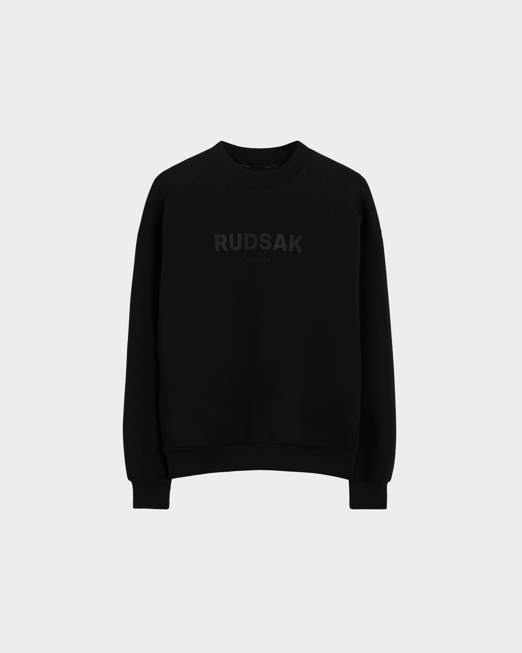 The BRYN - 9524007 Black W crewneck sweatshirt by Rudsak features subtle dark RUDSAK and EST. 1994 prints on the front, crafted from black cotton with genderless sizing—displayed on a light grey background for versatile everyday style.