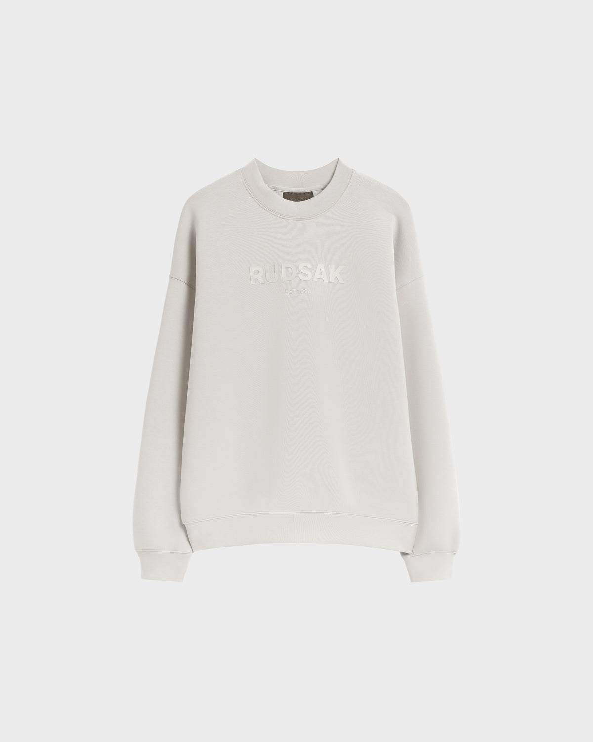 The BRYN - 9524007 Vanilla W by Rudsak is a plain white cotton crewneck sweatshirt with long sleeves, ribbed cuffs, and RUDSAK embroidered across the chest. It features a genderless fit and is shown against a plain white background.