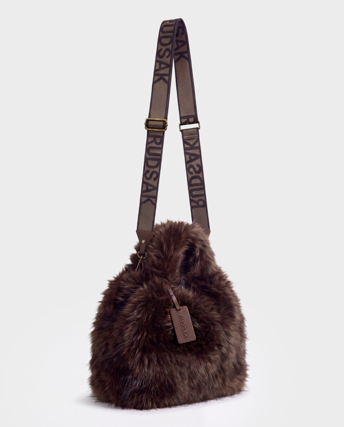 Rudsak CABAS - 8325545 Mix Expresso brown faux-fur bucket bag featuring a branded fabric shoulder strap, a matching leather luggage tag, and a statement accessory design.