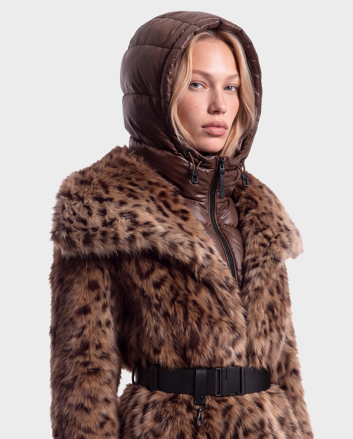 A person wearing a brown puffer hood over a Rudsak CHLOE - 8125619 Leopard vegan leather jacket cinched with a black buckled belt.