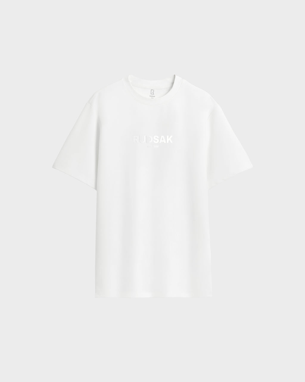 The Rudsak CASEY - 6525037 Optic White men’s T-shirt offers comfort with a plain white design and subtle RUDSAK branding on the chest, showcased against a light gray background.