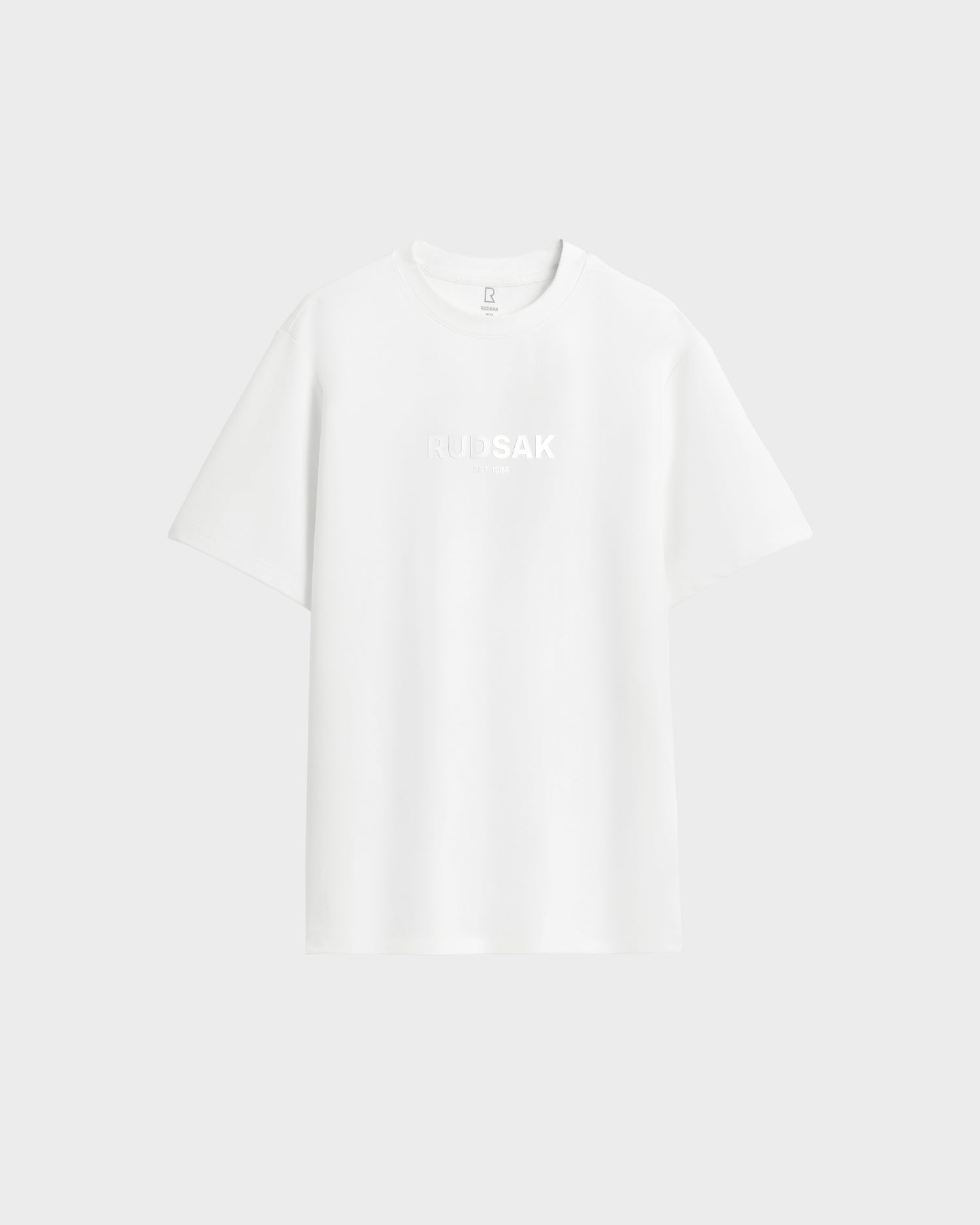 The Rudsak CASEY - 6525037 Optic White men’s T-shirt offers comfort with a plain white design and subtle RUDSAK branding on the chest, showcased against a light gray background.