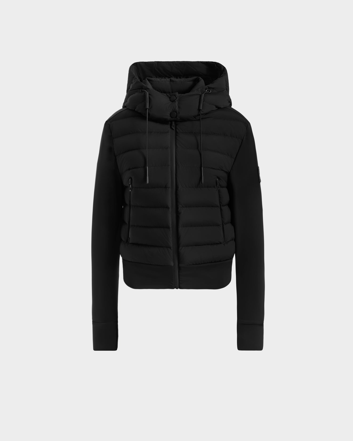 The Rudsak CASSA - 8125057 Black is a women’s puffer jacket with horizontal quilting, zip front, drawstring hood, and ribbed cuffs—ideal as a lightweight cropped layer for transitional weather. Shown on a plain light gray background.