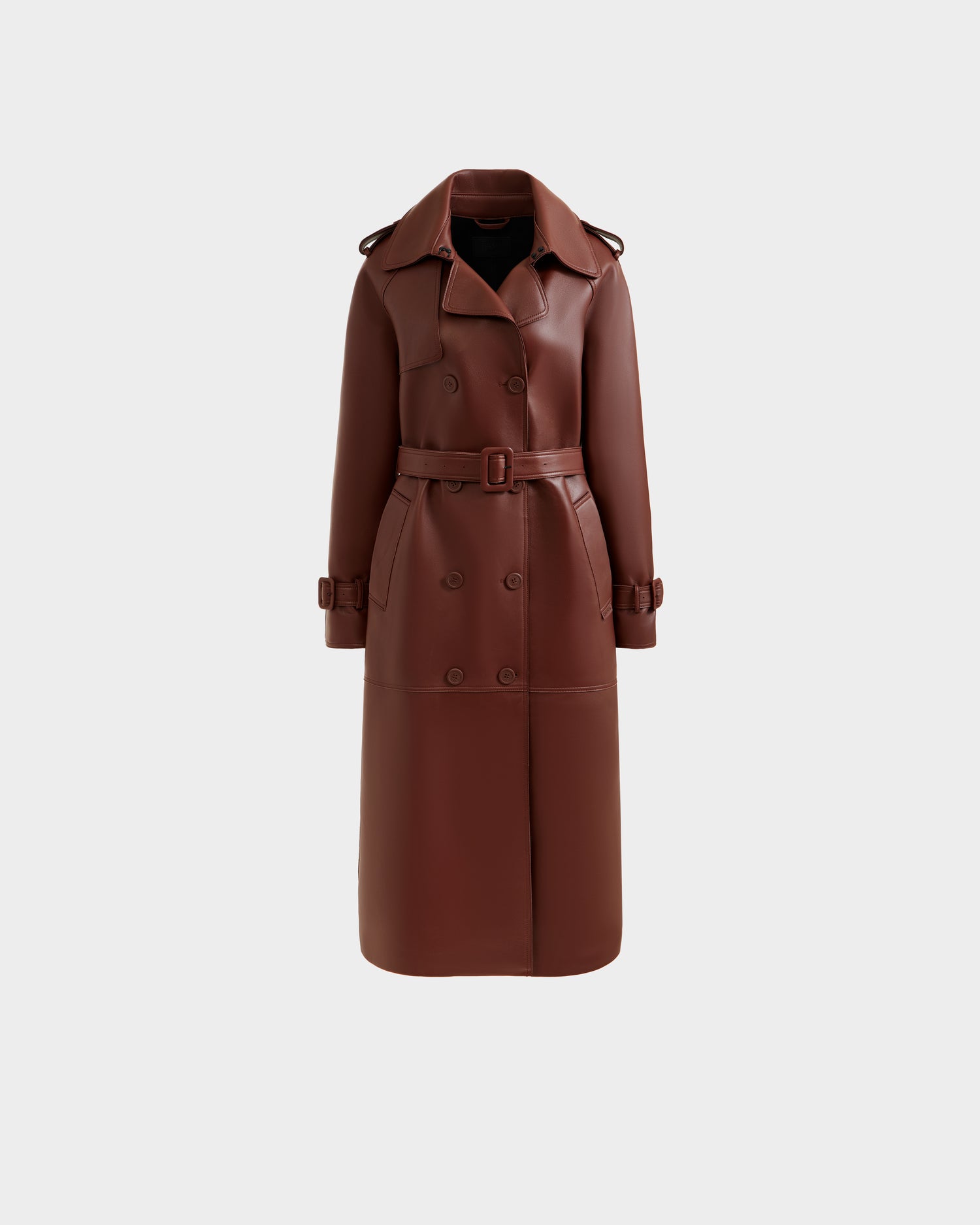 The Rudsak CASSIE L-B - 8125553 Rust women’s long trench coat in brown, with a double-breasted front, waist belt, wide lapels, and buttoned cuffs, is displayed against a plain light gray background.