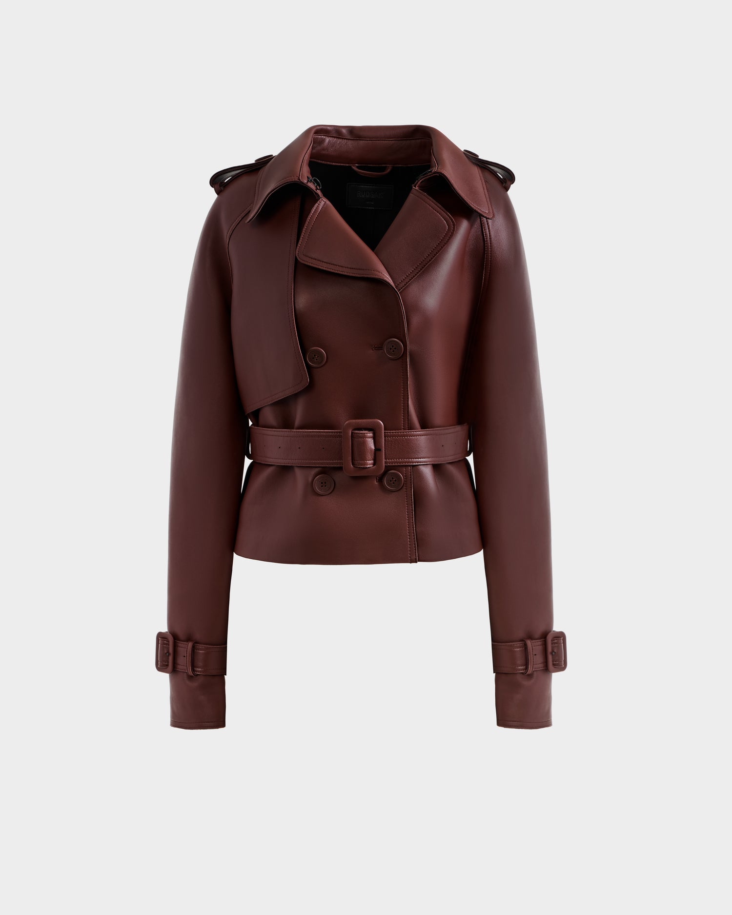 The Rudsak CASSIE S-B - 8125554 Rust is a cropped, double-breasted brown leather jacket with a wide collar, belted waist, shoulder epaulets, and belted cuffs, crafted from bonded leather and shown against a plain white background.