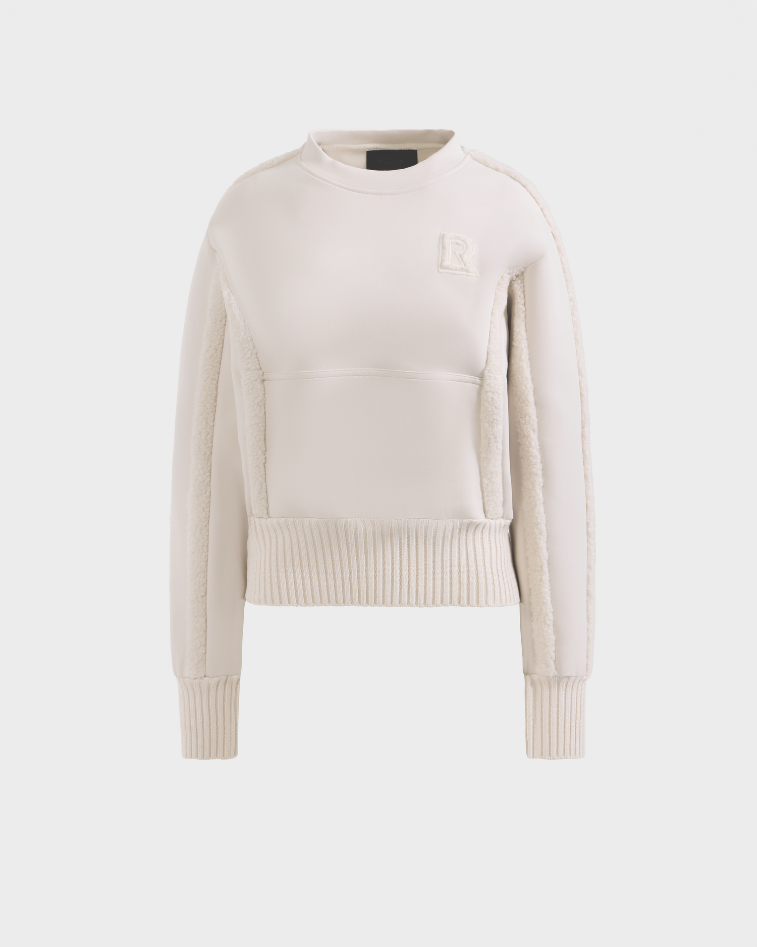 The Rudsak CHANA - 8525656 Vanilla is a cream women's crew neck sweatshirt with ribbed cuffs and hem, textured side panels, and an embroidered R logo on the chest, offering subtle après-ski chic style on a plain white background.