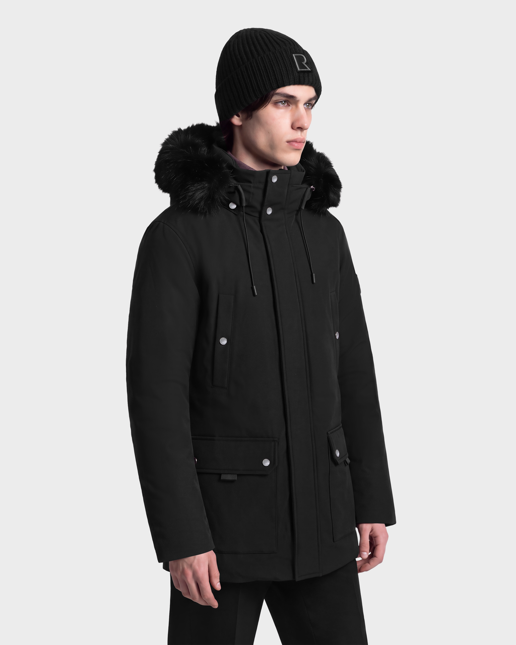A person wearing an EDWARD - 6126501 Black Rudsak parka with a faux-fur trim and a black knit beanie.