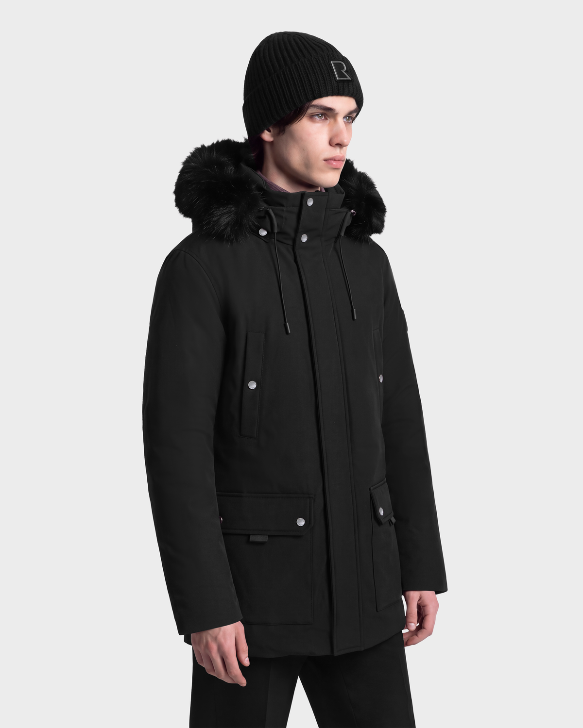 A person wearing an EDWARD - 6126501 Black Rudsak parka with a faux-fur trim and a black knit beanie.