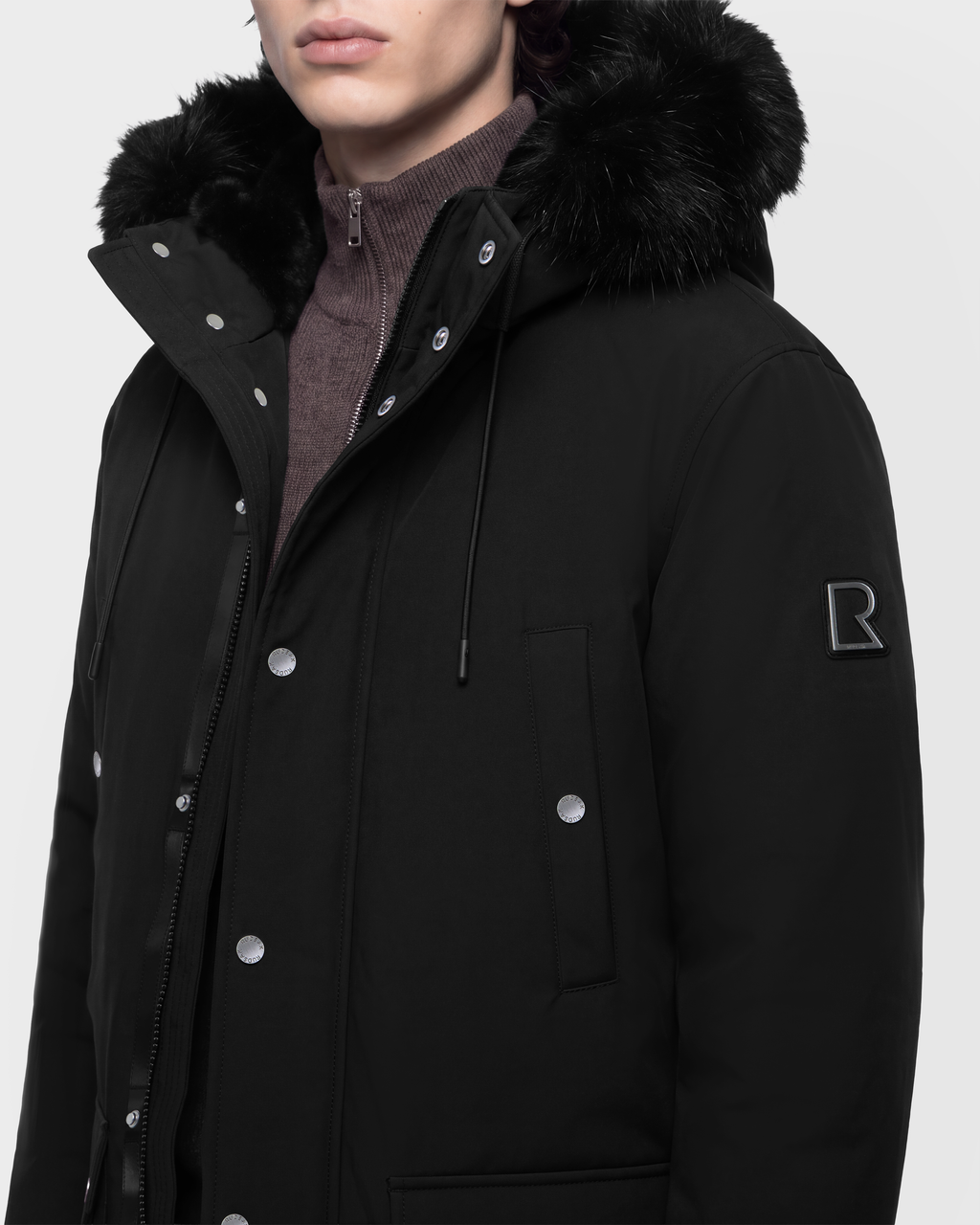 Black Rudsak EDWARD - 6126501 winter parka with a fur-trimmed hood and a metallic logo patch on the sleeve.