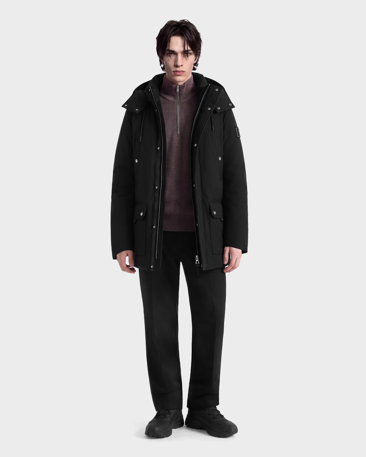 A person wearing an EDWARD - 6126501 Black duck down winter parka over a mauve zip-up sweater, black trousers, and black sneakers.