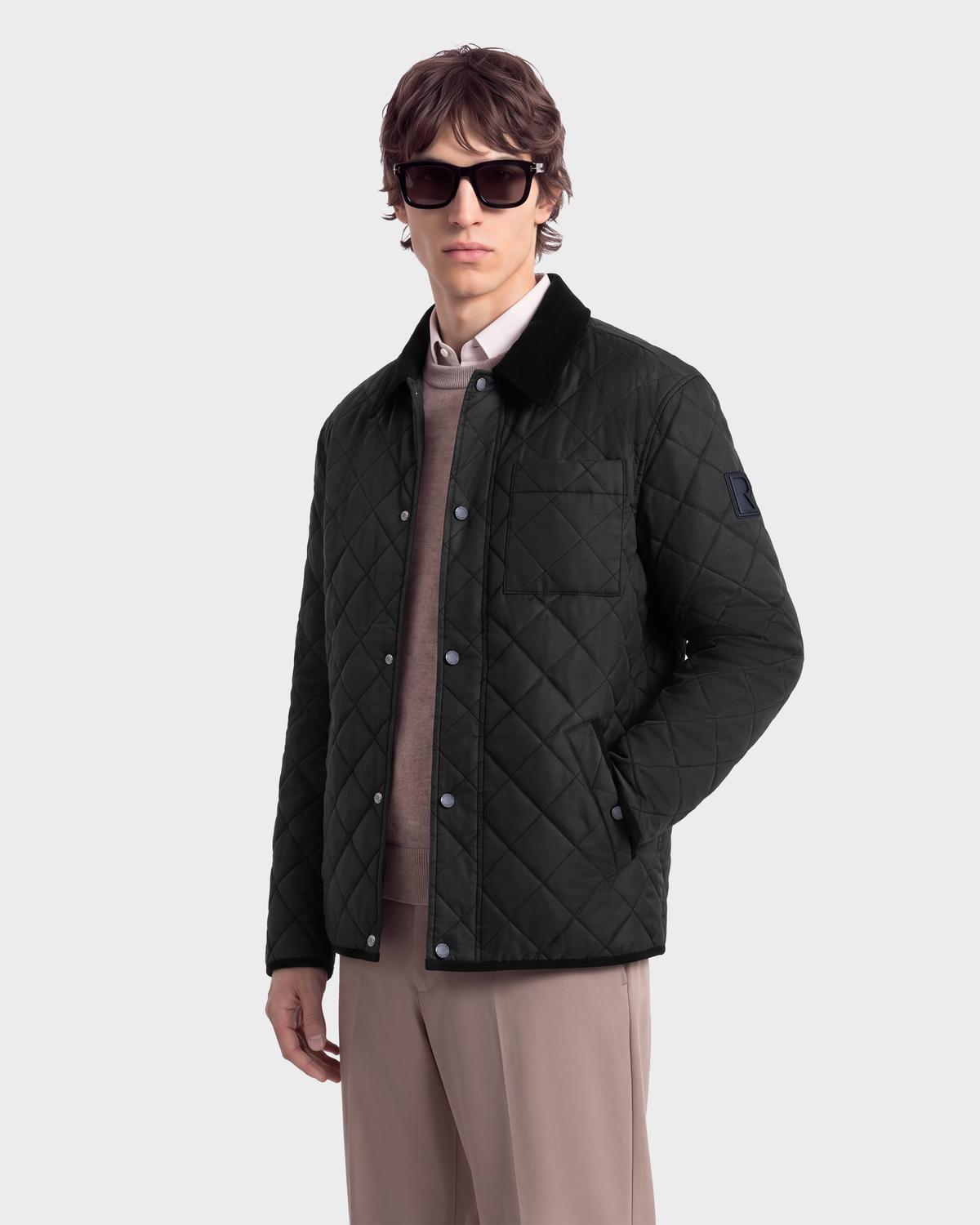 A man wears a black Rudsak MONTY - 6126722 Black quilted snap-front jacket with a dark collar over a light-colored sweater and dress pants.