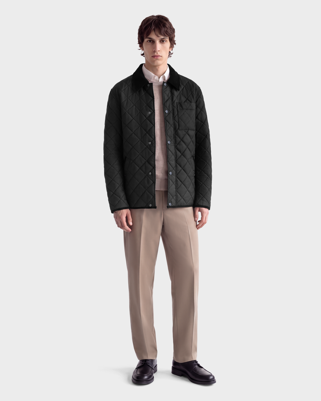 A man wearing a MONTY - 6126722 Black quilted jacket with a collar, a beige sweater over a collared shirt, tan trousers, and black loafers.