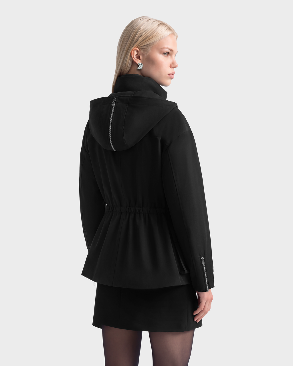 A person wearing a black Rudsak ROSALINDA - 8126523 Black insulated jacket with a cinched waist, a back hood zipper, and zippered cuffs.