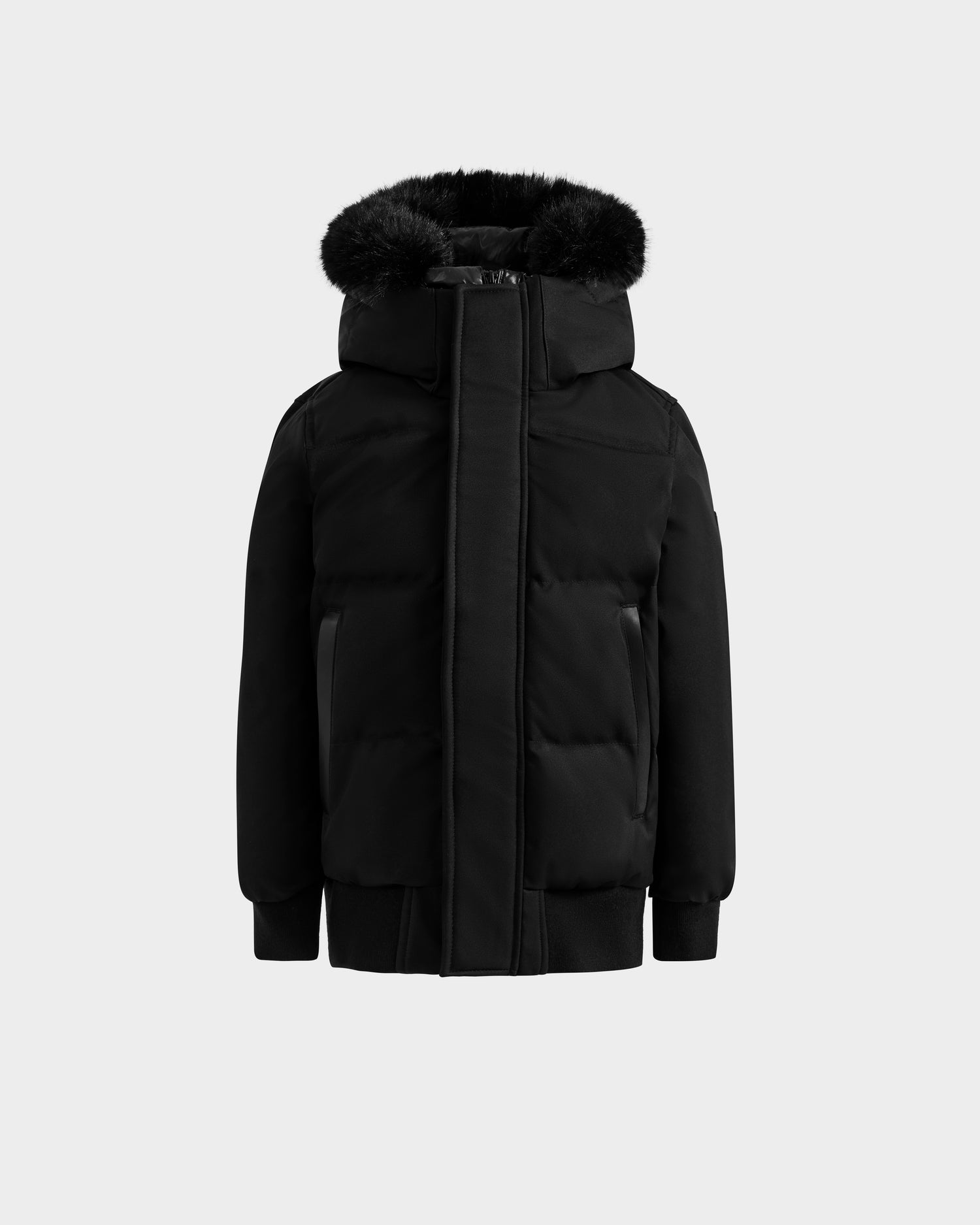 The Rudsak DALLAS K - K125501 Black is a black puffer winter jacket with a hood featuring black faux fur trim, front zipper and snap closures, plus ribbed cuffs and hem, shown on a plain light grey background.