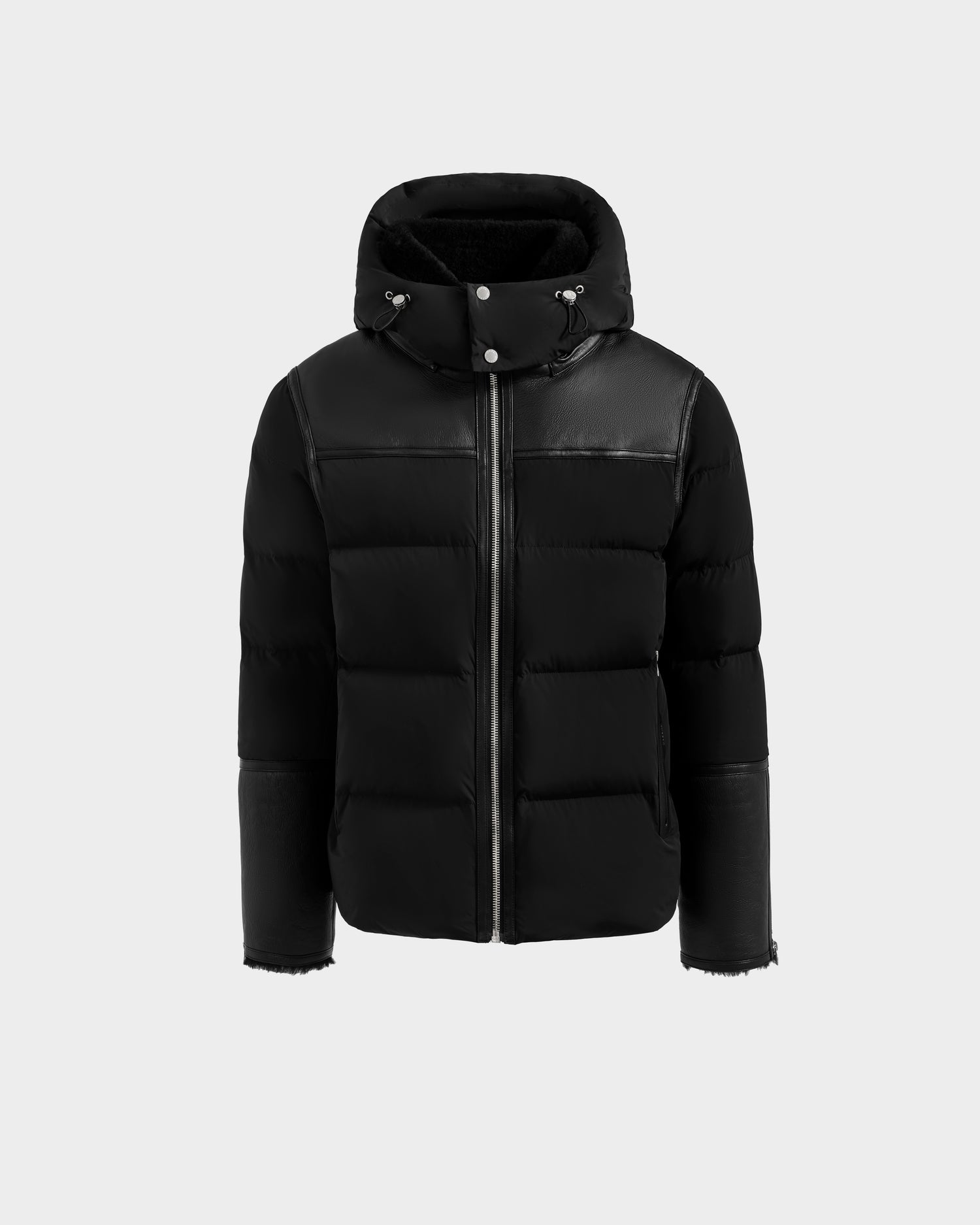 The Rudsak DAVID - M125508 Black is a black down puffer jacket with a hood, front zipper, and leather-like panels on the shoulders and sleeves, shown against a plain light gray background—ideal for stylish winter wear.