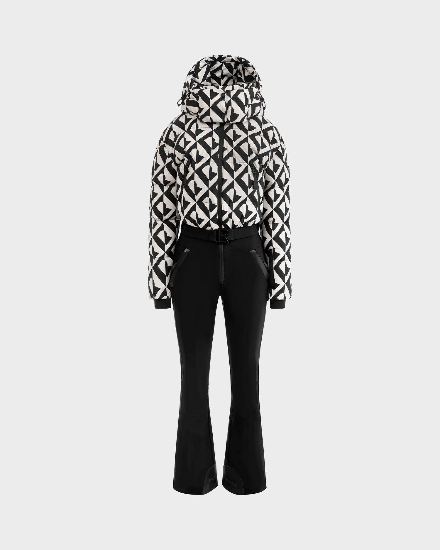 The Rudsak DINARA - 8125600 Vanilla Monogram women’s ski suit features a black and white geometric monogram pattern with a hood, paired with solid black fitted pants, shown on a seamless white background.