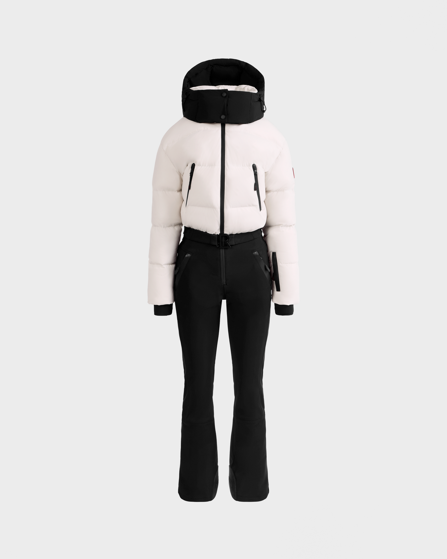 The DINARA - 8125600 Vanilla by Rudsak is a stylish women’s ski suit with a white puffer jacket, black zipper details, fitted black pants, and RECCO® rescue technology, shown on a plain light grey background.