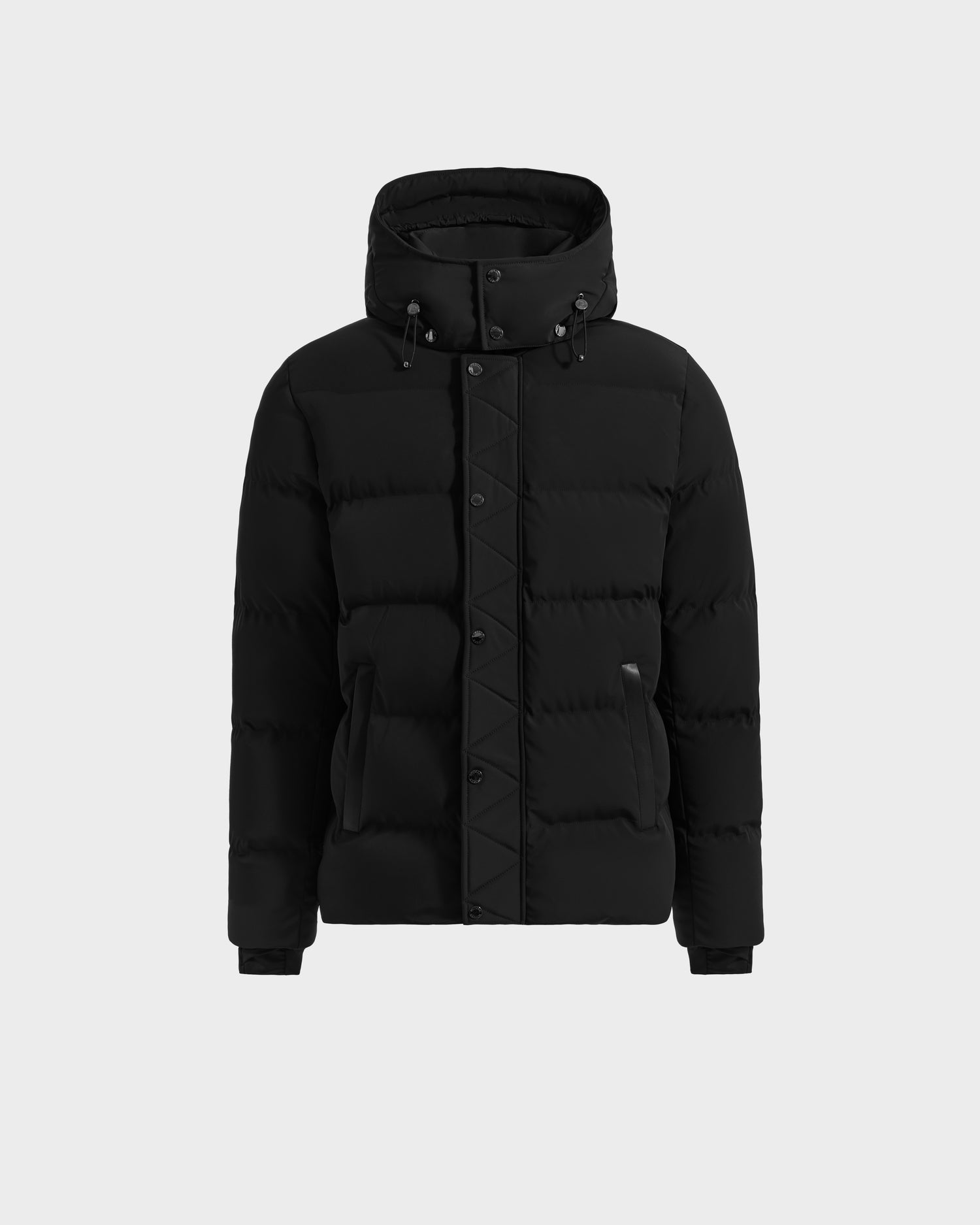 The Rudsak DOMINIC - 6125041 Black is a black hooded winter jacket with front button and zipper closures, two side pockets, and a quilted recycled shell, shown against a plain light gray background.