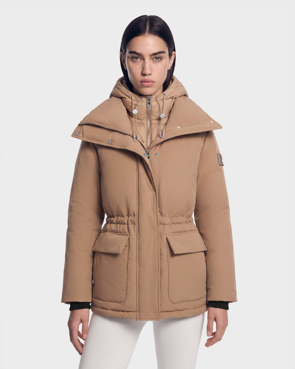 A person wearing a camel-colored Rudsak BHIMA - 8126515 hooded puffer jacket with a wide collar and cinched waist.