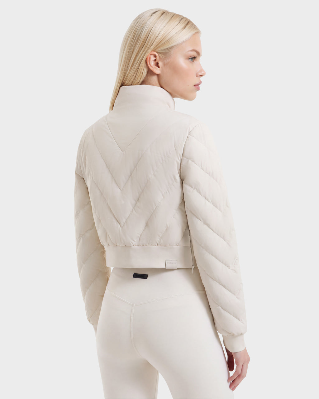 A model seen from the back wearing a cropped, cream-colored quilted KATYA - 8526531 Vanilla après-ski layer.
