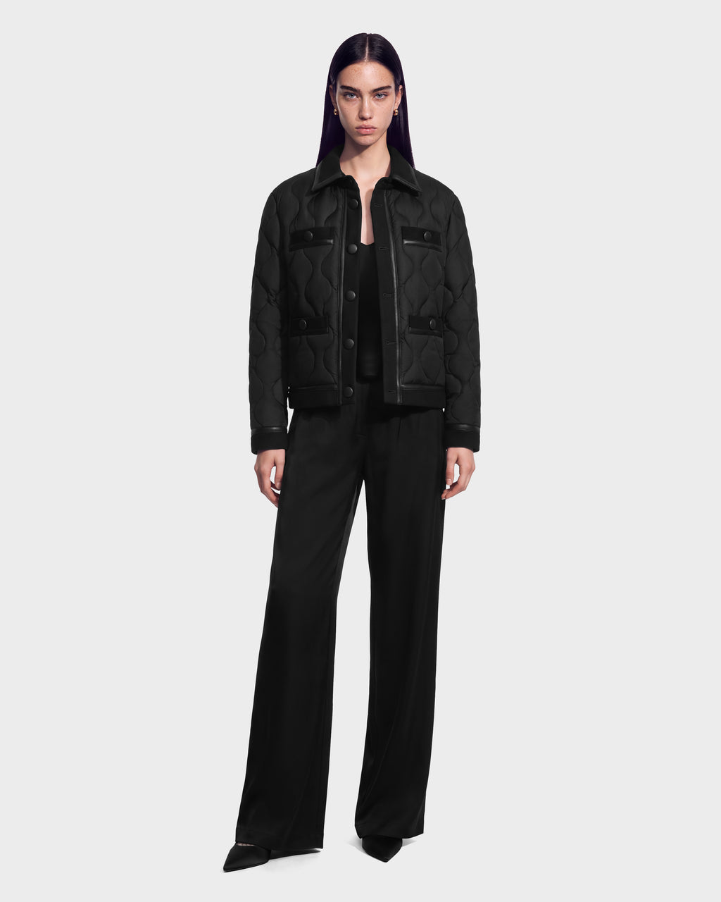 A model wearing a black JOLIE - 8125036 Black RUDSAK quilted down jacket with leather accents and wide-leg trousers.