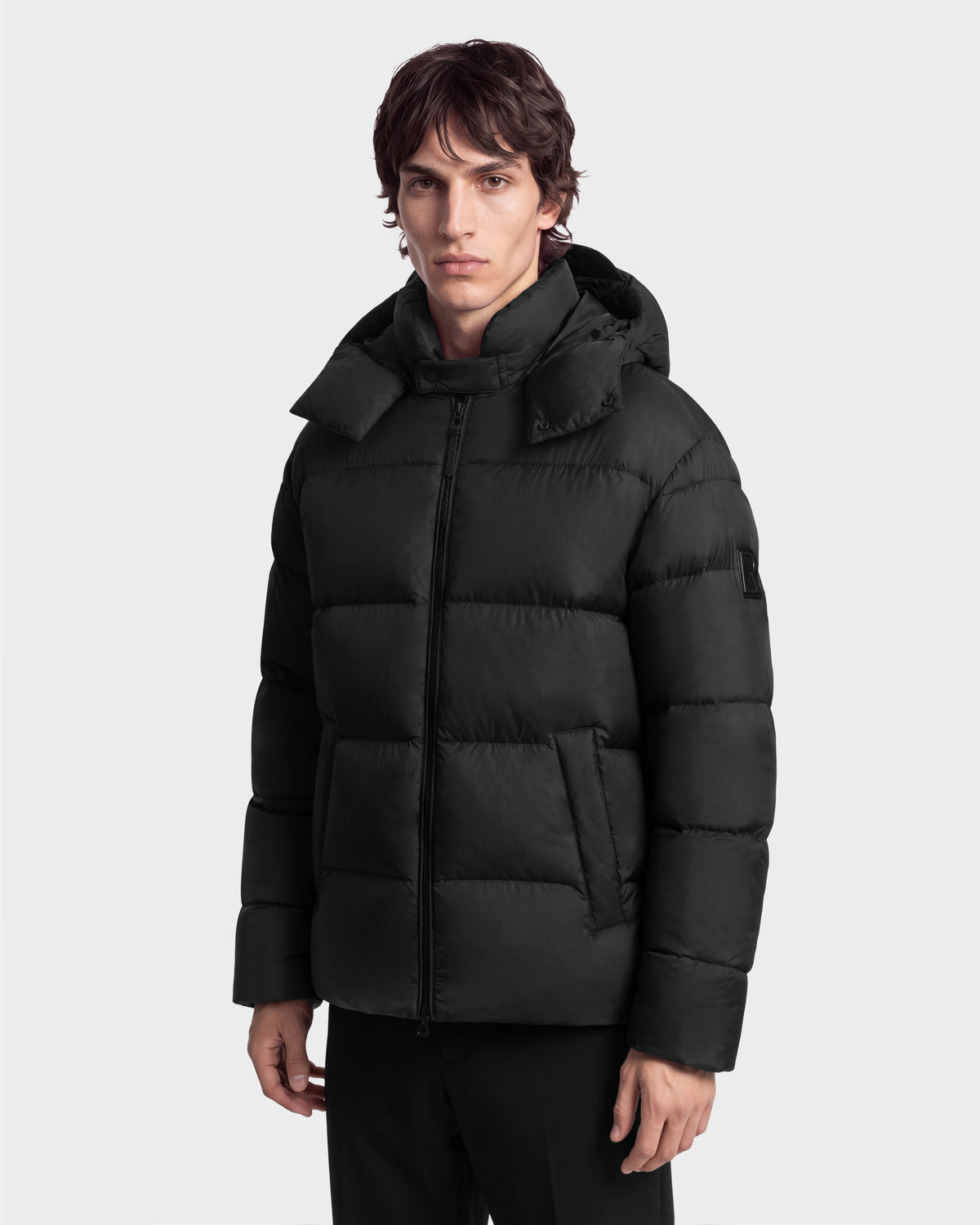 A man wearing a black Rudsak JASON - 6126803 Black hooded puffer jacket with a front zipper, designed as a classic winter coat.