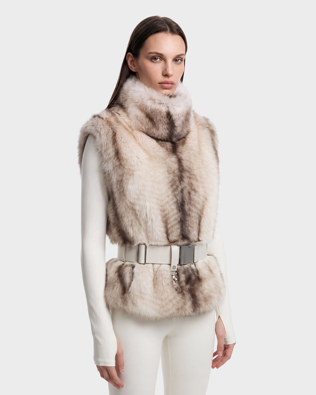 A model wears the MAULIN - 8524611 Mix Vanilla faux fur vest with a high collar, cinched by a wide white belt over a mock-neck pullover and matching leggings.