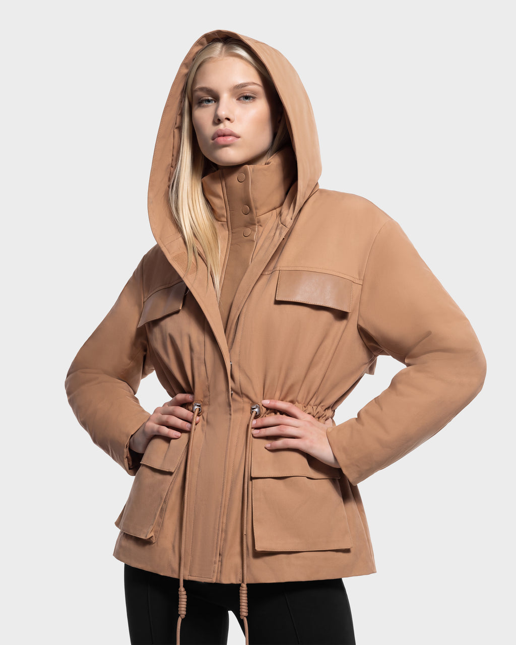 A person wearing a camel-colored Rudsak ROSALINDA - 8126523 Camel hooded jacket with a high collar and a drawstring waist.