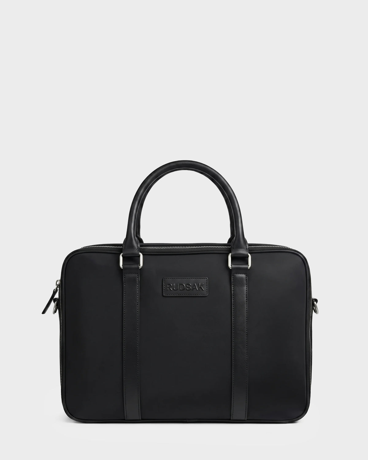 The HENRY N - 9326056 Black by Rudsak is a rectangular black leather briefcase featuring two handles, silver hardware, and the Rudsak logo embossed at the front center. The bag is displayed against a plain white background.