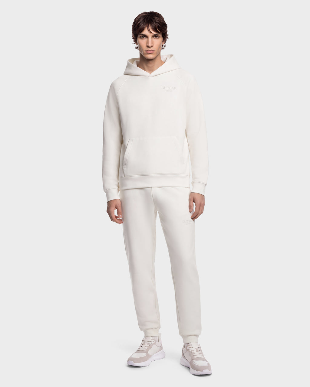A man wearing a RUDSAK BRIAR - 9525001 Vanilla M off-white unisex hoodie, matching sweatpants, and sneakers.