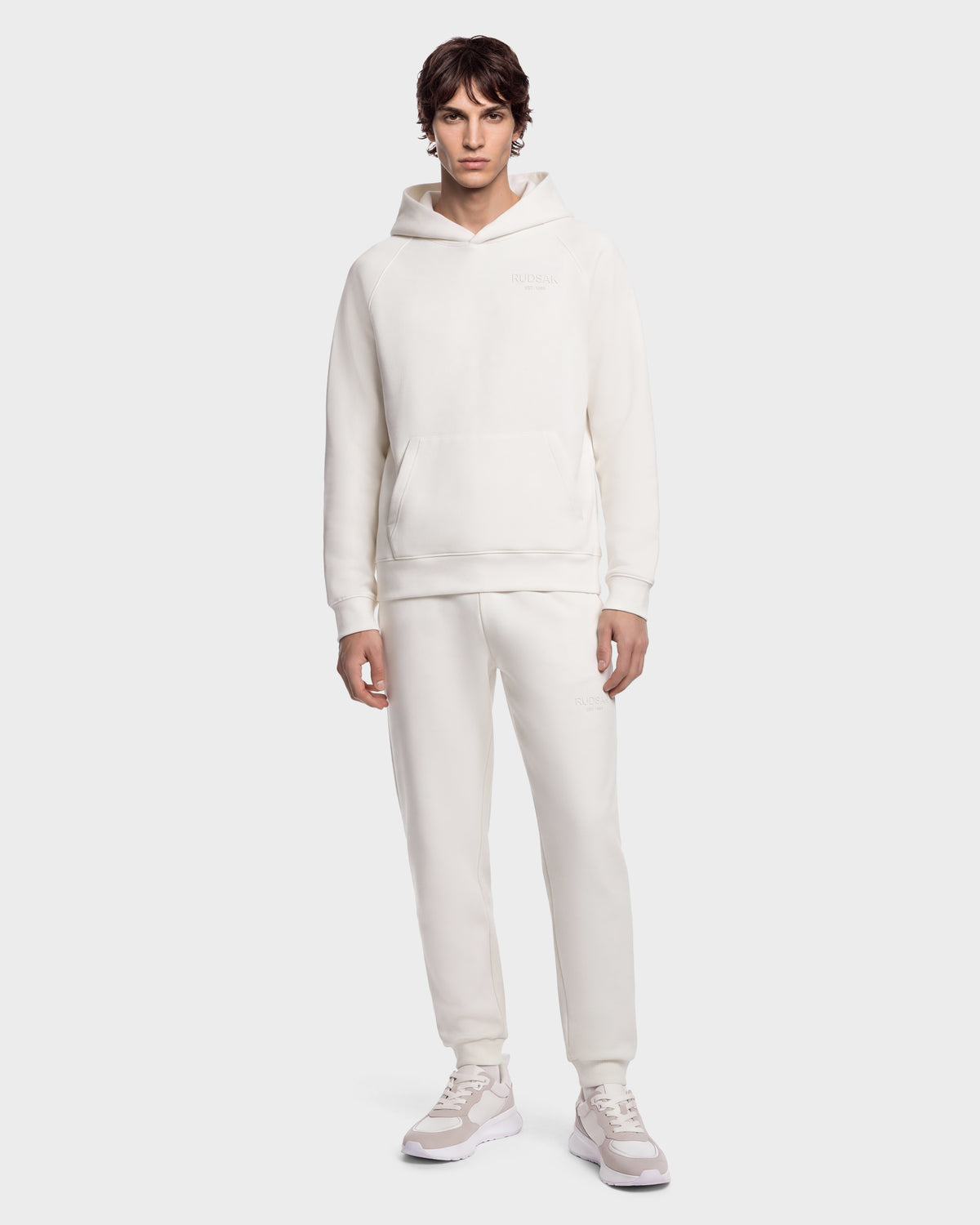 A man wearing a RUDSAK BRIAR - 9525001 Vanilla M off-white unisex hoodie, matching sweatpants, and sneakers.