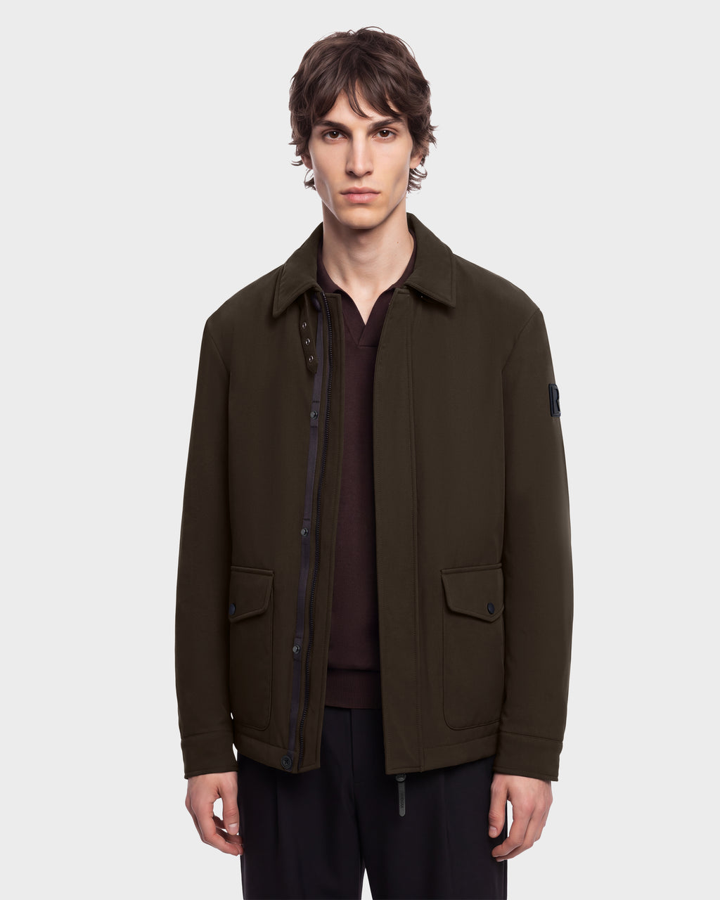 A man wears an olive green ANTOINE - 6126506 utility jacket over a dark brown polo shirt.